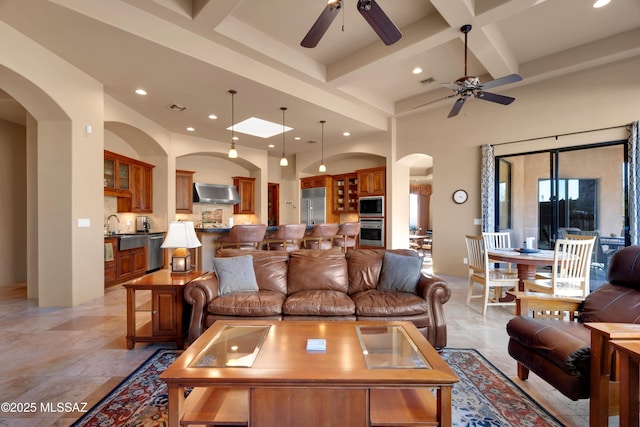 living room featuring beamed ceiling, ceiling fan, coffered ceiling, and a high ceiling