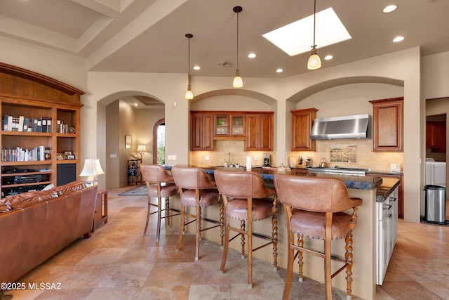 kitchen with wall chimney range hood, decorative backsplash, washer and dryer, and a breakfast bar