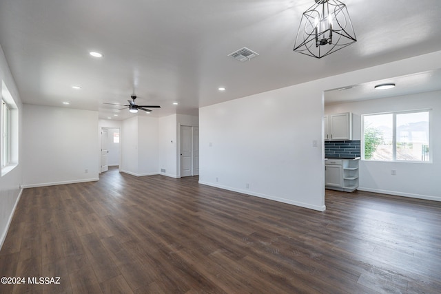 unfurnished living room featuring ceiling fan with notable chandelier and dark hardwood / wood-style flooring