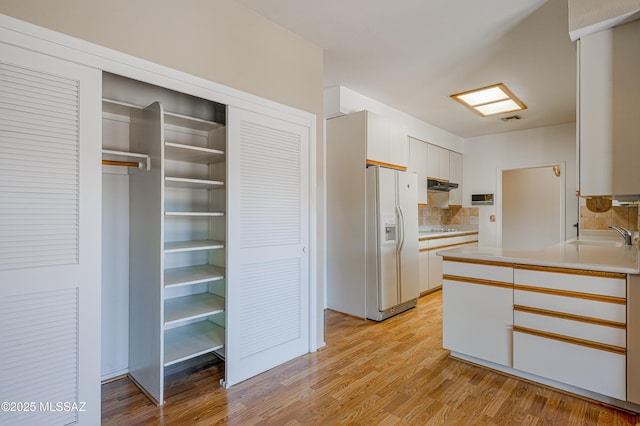 kitchen featuring sink, white cabinetry, white fridge with ice dispenser, light hardwood / wood-style floors, and decorative backsplash