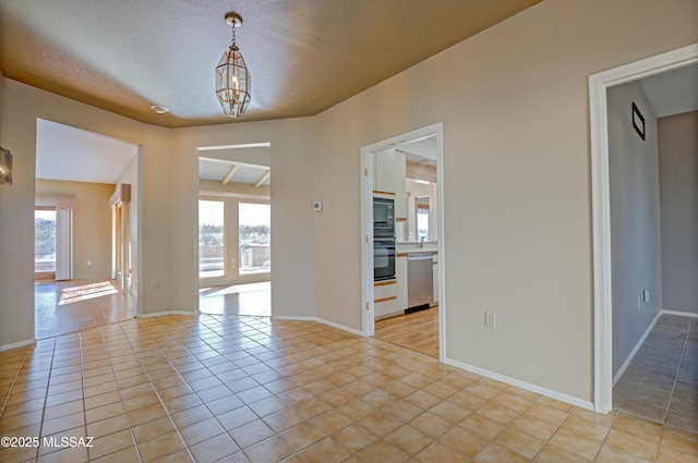 spare room featuring a notable chandelier, a textured ceiling, and light tile patterned floors