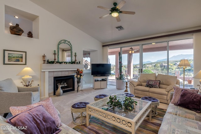 carpeted living room with ceiling fan, a tiled fireplace, and vaulted ceiling