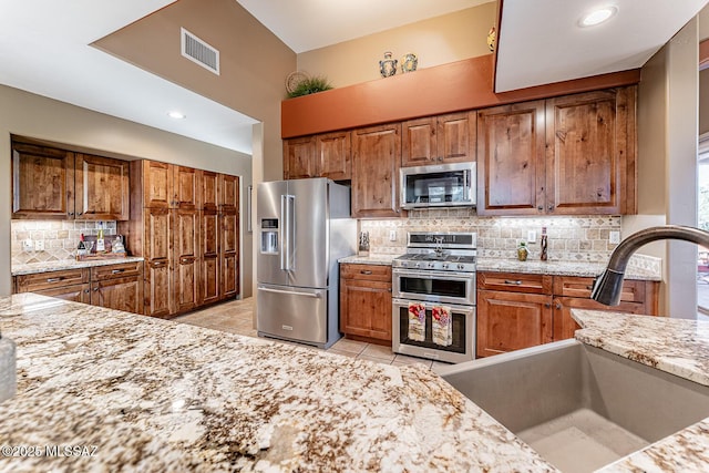 kitchen featuring tasteful backsplash, stainless steel appliances, light stone countertops, and sink