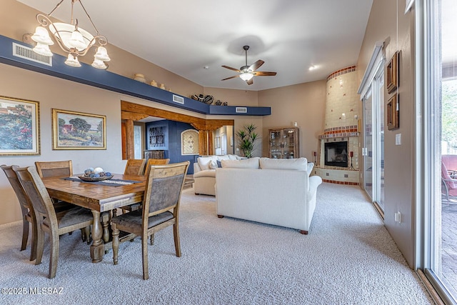 carpeted dining area featuring ceiling fan with notable chandelier and a brick fireplace