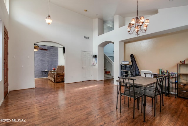 dining room with ceiling fan with notable chandelier, dark hardwood / wood-style floors, and a high ceiling