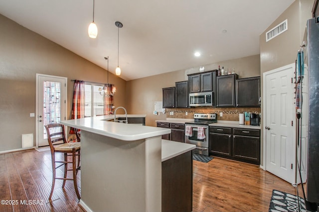 kitchen featuring a breakfast bar, tasteful backsplash, hanging light fixtures, stainless steel appliances, and a center island with sink