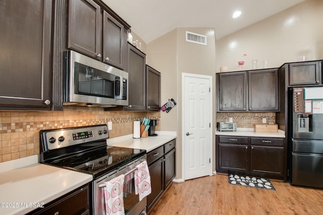 kitchen featuring appliances with stainless steel finishes, lofted ceiling, decorative backsplash, dark brown cabinets, and light wood-type flooring