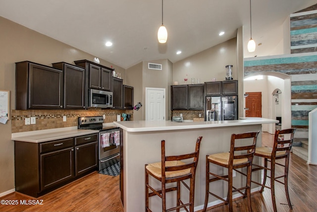 kitchen with a kitchen bar, vaulted ceiling, appliances with stainless steel finishes, pendant lighting, and a kitchen island with sink