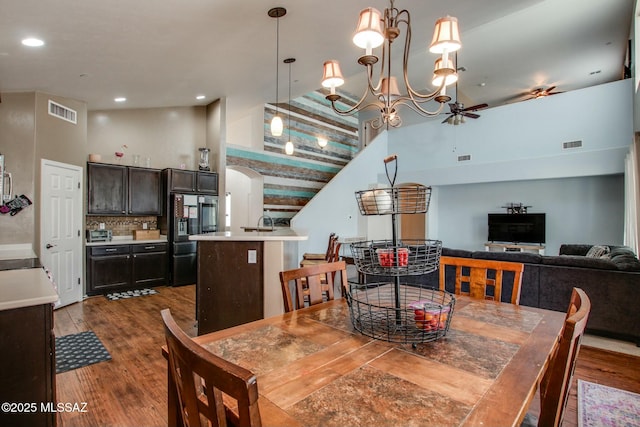 dining room with dark hardwood / wood-style flooring, ceiling fan with notable chandelier, and high vaulted ceiling