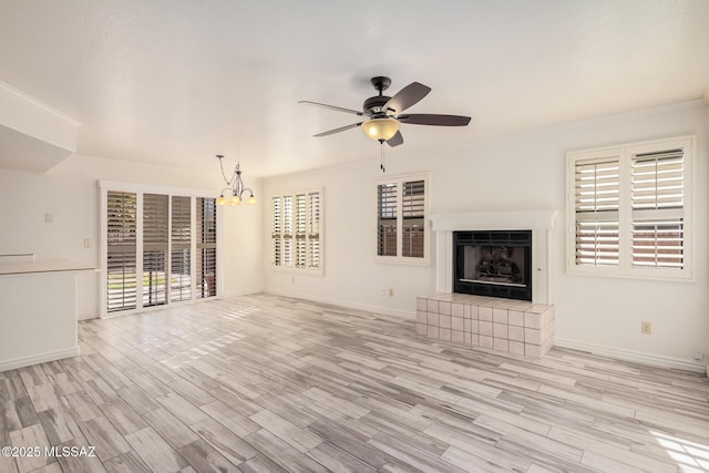 unfurnished living room featuring light wood-type flooring, ceiling fan with notable chandelier, a tile fireplace, and crown molding