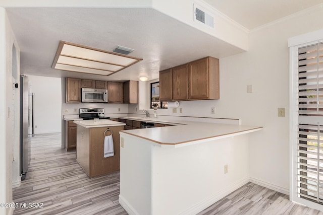 kitchen featuring kitchen peninsula, ornamental molding, stainless steel appliances, light hardwood / wood-style flooring, and a kitchen island