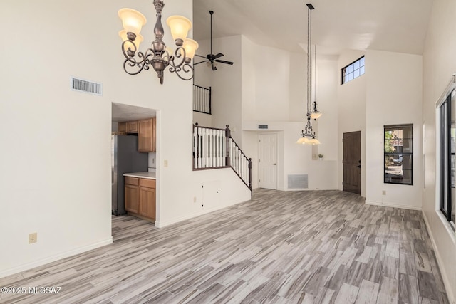 unfurnished living room with a towering ceiling, light hardwood / wood-style floors, and ceiling fan with notable chandelier