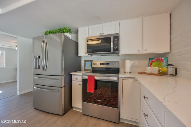 kitchen with white cabinets, light wood-type flooring, ceiling fan, light stone countertops, and appliances with stainless steel finishes