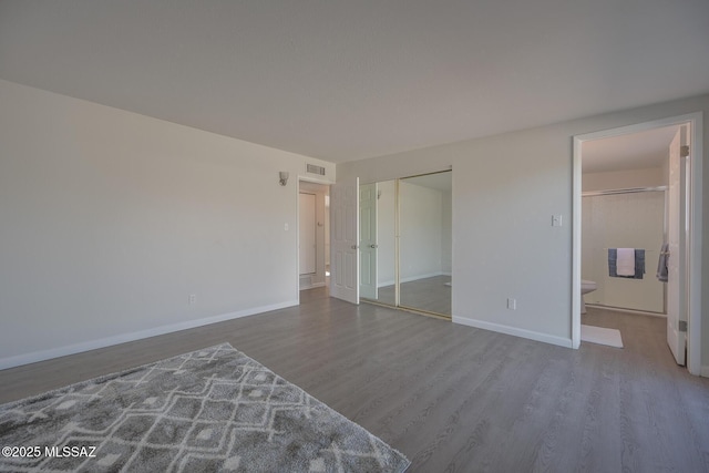 unfurnished bedroom with wood-type flooring, a closet, and connected bathroom