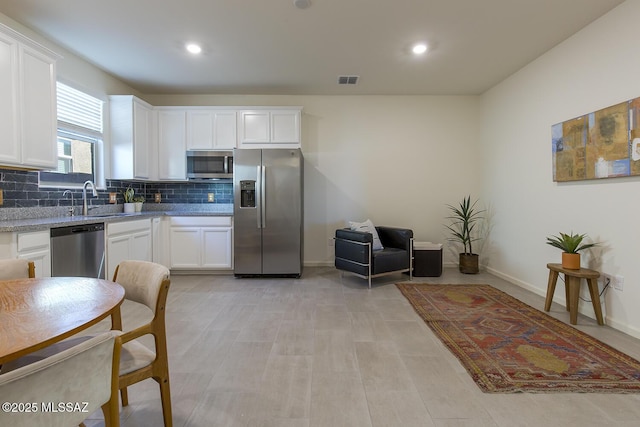 kitchen with stainless steel appliances, light stone countertops, sink, white cabinetry, and backsplash