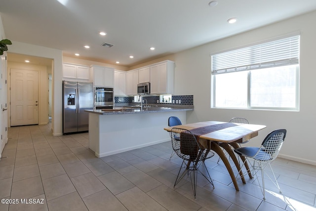 kitchen featuring kitchen peninsula, stainless steel appliances, dark stone counters, and white cabinets