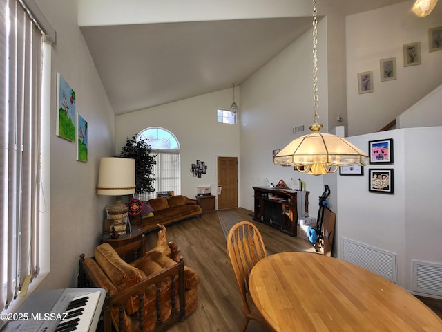 dining area with hardwood / wood-style floors, high vaulted ceiling, and an inviting chandelier