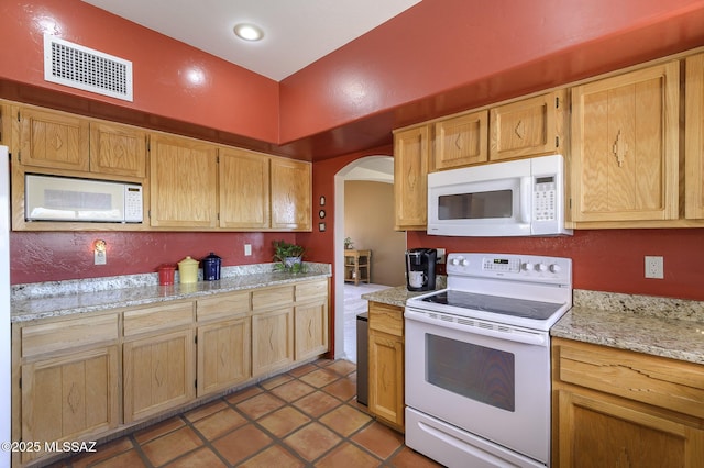 kitchen with light tile patterned flooring, light stone countertops, and white appliances