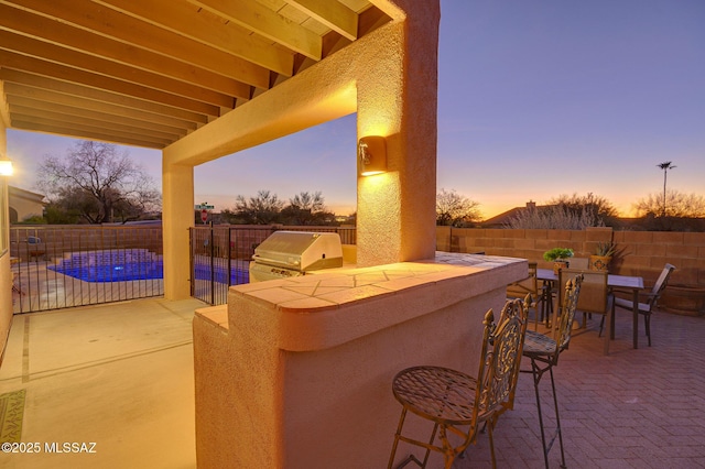 patio terrace at dusk with a fenced in pool, a grill, area for grilling, and a bar