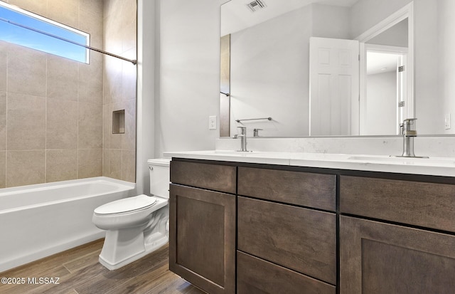 full bathroom with visible vents, toilet, wood finished floors, a sink, and double vanity