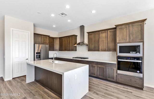 kitchen featuring visible vents, a sink, wall chimney range hood, appliances with stainless steel finishes, and light wood-style flooring