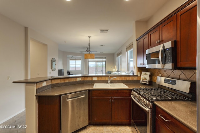 kitchen featuring kitchen peninsula, appliances with stainless steel finishes, backsplash, ceiling fan, and sink