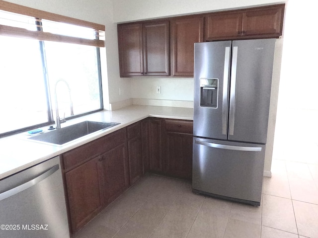 kitchen featuring dark brown cabinetry, sink, light tile patterned floors, and appliances with stainless steel finishes