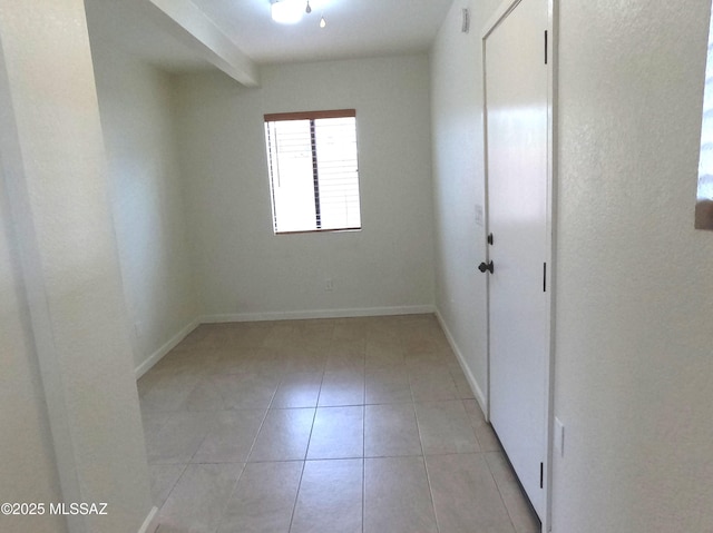 tiled spare room featuring beamed ceiling