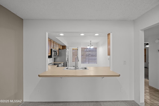 kitchen with sink, a textured ceiling, kitchen peninsula, stainless steel appliances, and a chandelier