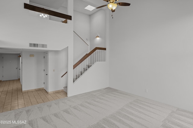 unfurnished living room featuring a skylight, ceiling fan, a towering ceiling, and light tile patterned floors