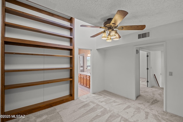 unfurnished bedroom featuring ceiling fan, ensuite bathroom, light carpet, and a textured ceiling