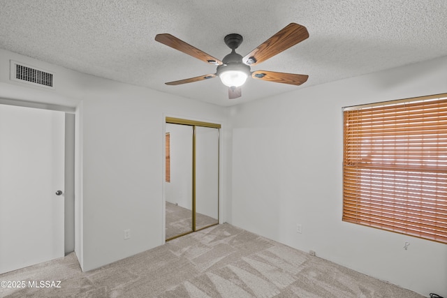 unfurnished bedroom featuring ceiling fan, a closet, light carpet, and a textured ceiling