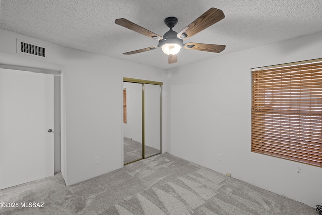 unfurnished bedroom with ceiling fan, a textured ceiling, light carpet, and a closet