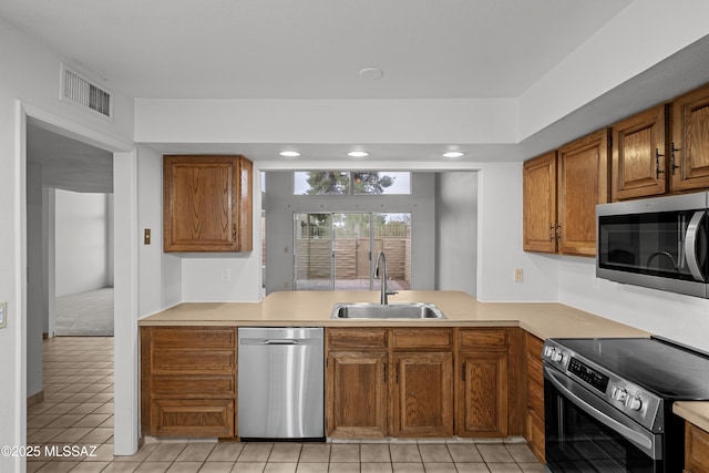 kitchen with light tile patterned flooring, stainless steel appliances, kitchen peninsula, and sink