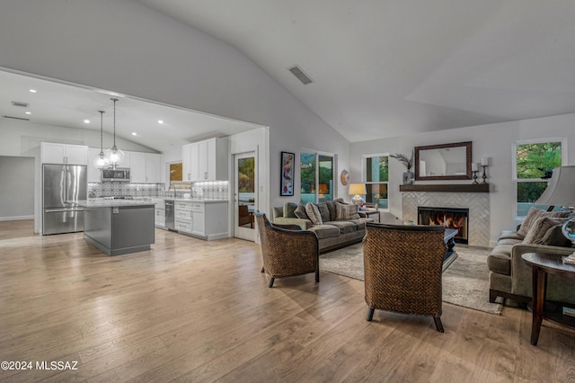 living room with plenty of natural light, a tiled fireplace, light hardwood / wood-style flooring, and vaulted ceiling