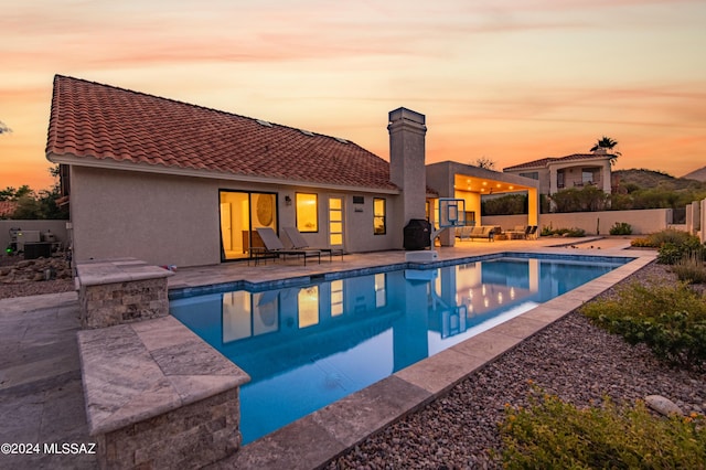 pool at dusk featuring a grill, a patio, and an outdoor hangout area