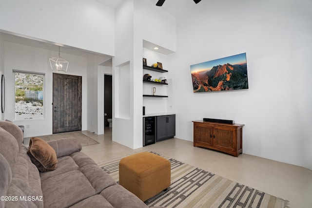 living area featuring beverage cooler, a chandelier, bar, ceiling fan, and a towering ceiling