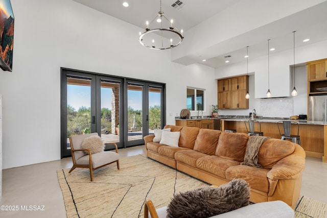 living room featuring french doors, concrete flooring, a chandelier, recessed lighting, and a high ceiling