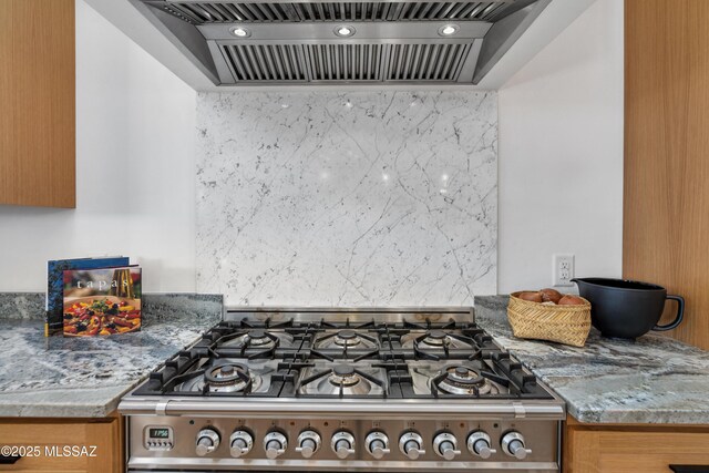 kitchen with gas range, premium range hood, backsplash, and brown cabinetry