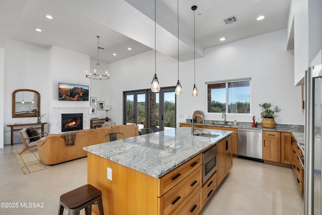 kitchen with stainless steel appliances, a towering ceiling, finished concrete floors, a glass covered fireplace, and a kitchen bar