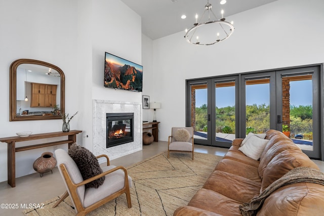 living area with a towering ceiling, finished concrete floors, a high end fireplace, a chandelier, and french doors