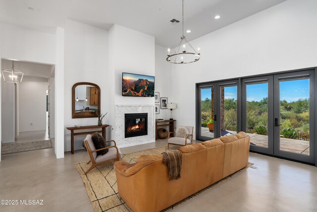 living area featuring a chandelier, concrete floors, a towering ceiling, a fireplace, and recessed lighting