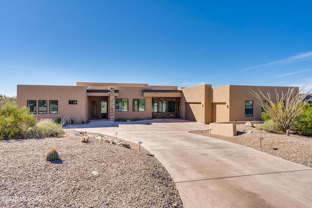 pueblo-style home with stucco siding, driveway, and an attached garage