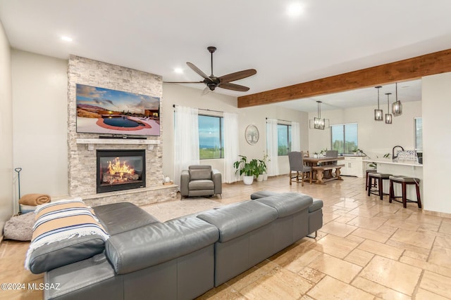 living room featuring beamed ceiling, ceiling fan with notable chandelier, sink, and a fireplace