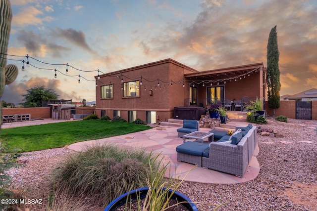 back house at dusk with a fire pit, a patio area, a hot tub, and a lawn