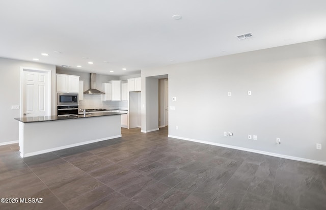 kitchen with stainless steel appliances, tasteful backsplash, white cabinets, a center island with sink, and wall chimney exhaust hood