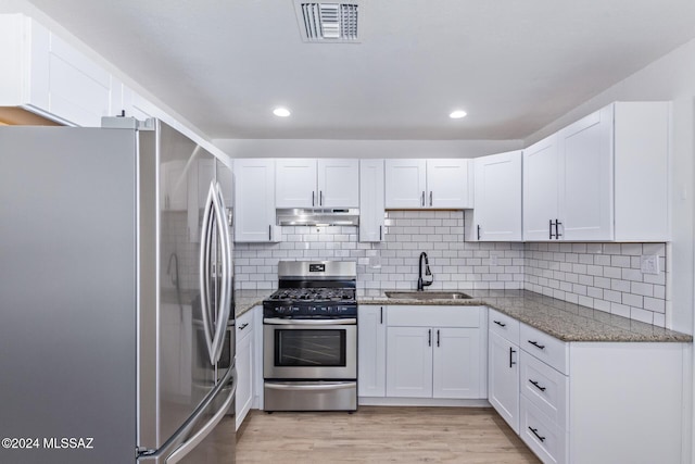 kitchen with stainless steel appliances, white cabinetry, stone countertops, and sink