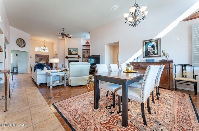 dining space featuring a towering ceiling, ceiling fan with notable chandelier, and light wood-type flooring