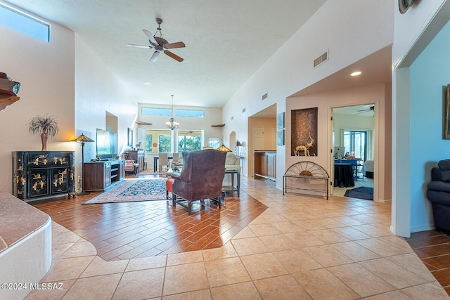 tiled living room with ceiling fan with notable chandelier and a high ceiling