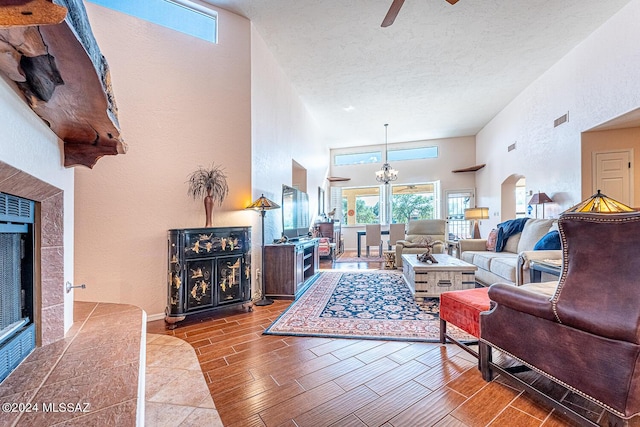 living room with a towering ceiling, ceiling fan with notable chandelier, a textured ceiling, and a fireplace